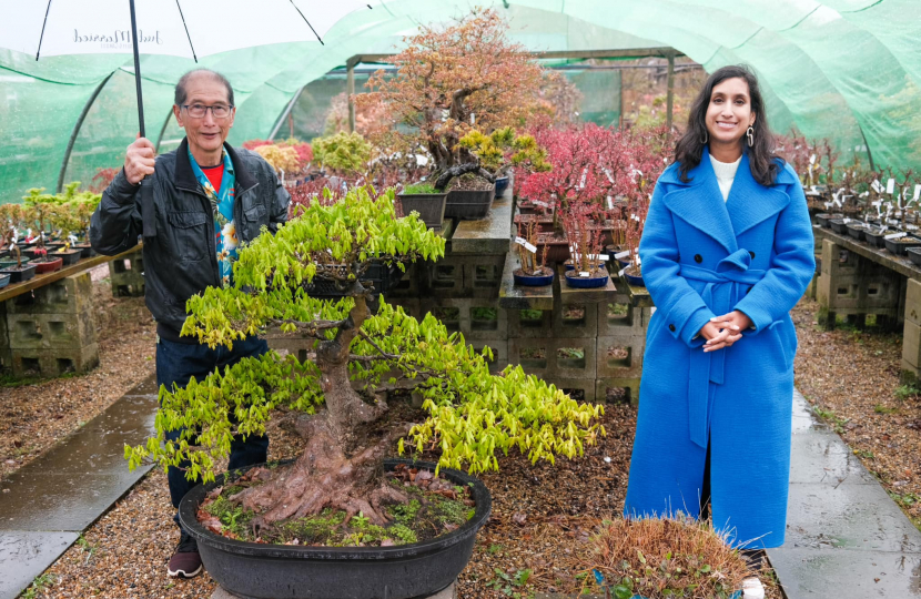 Claire is standing with Peter Chan, next to a large bonsai tree.