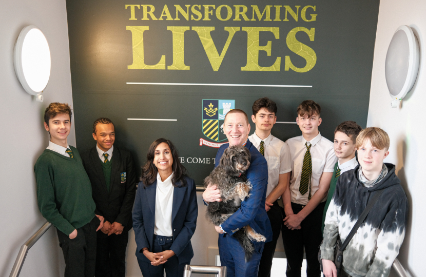 Claire is standing in the stairwell of Sunnydown School with Mr Jensen and students. Mr Jensen is holding a dog.